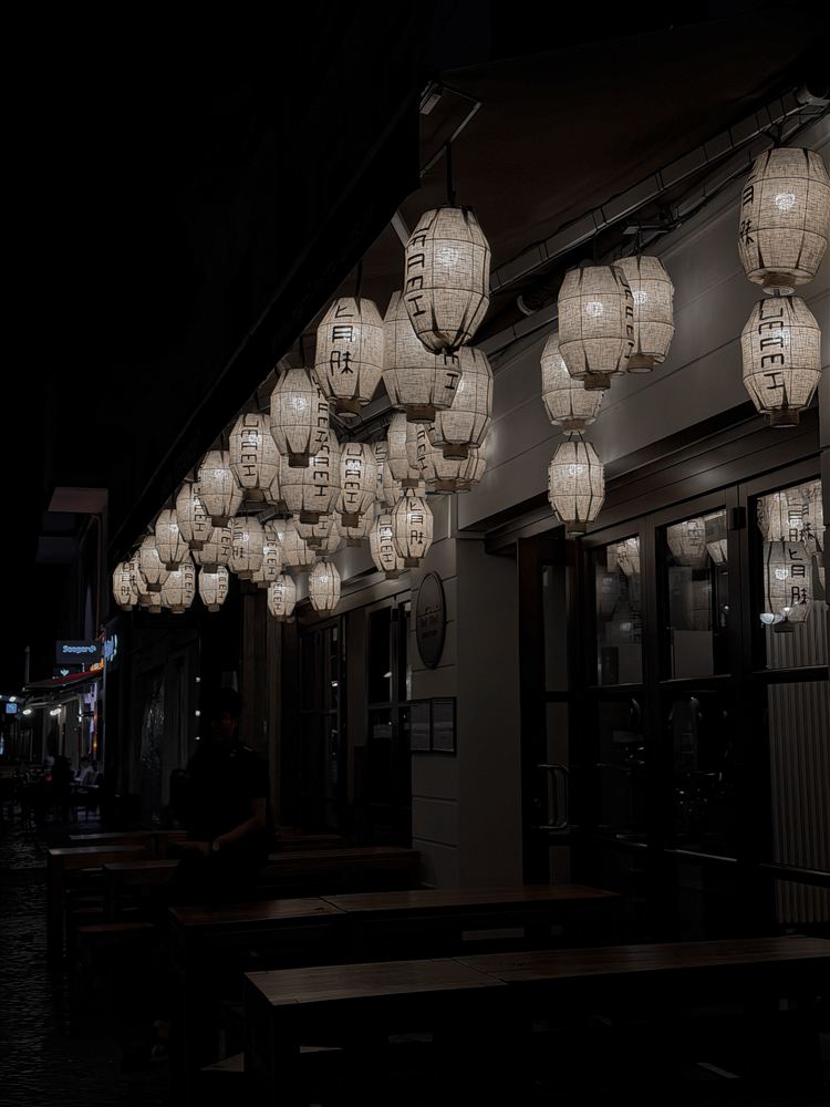 Rows of glowing lanterns above the outdoor wooden tables at Umami Ku’damm in Berlin at night.